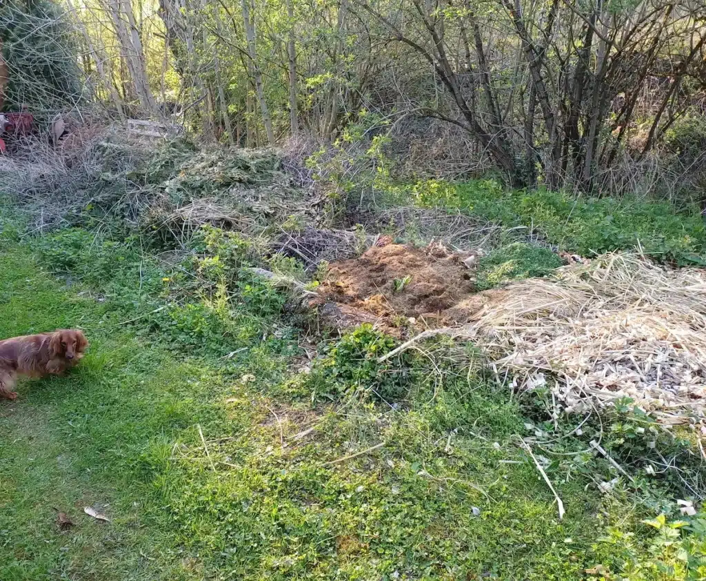 Composteur maison de grande taille réalisé avec des troncs d'arbres récupérés, rempli de matières organiques et déchets végétaux dans une propriété en Moselle.